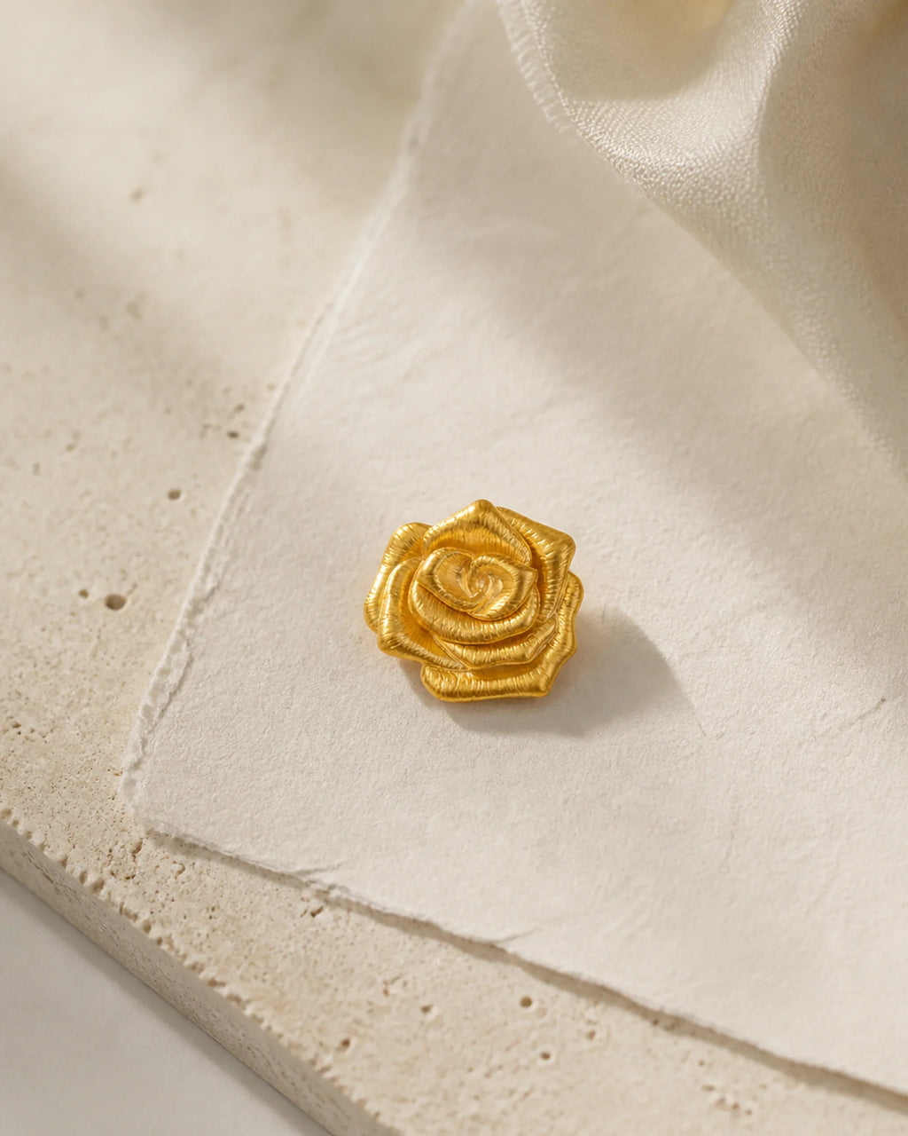 Taimi Mini Gold Camellia Brooch resting on ivory handmade paper and pale limestone in an original studio still life