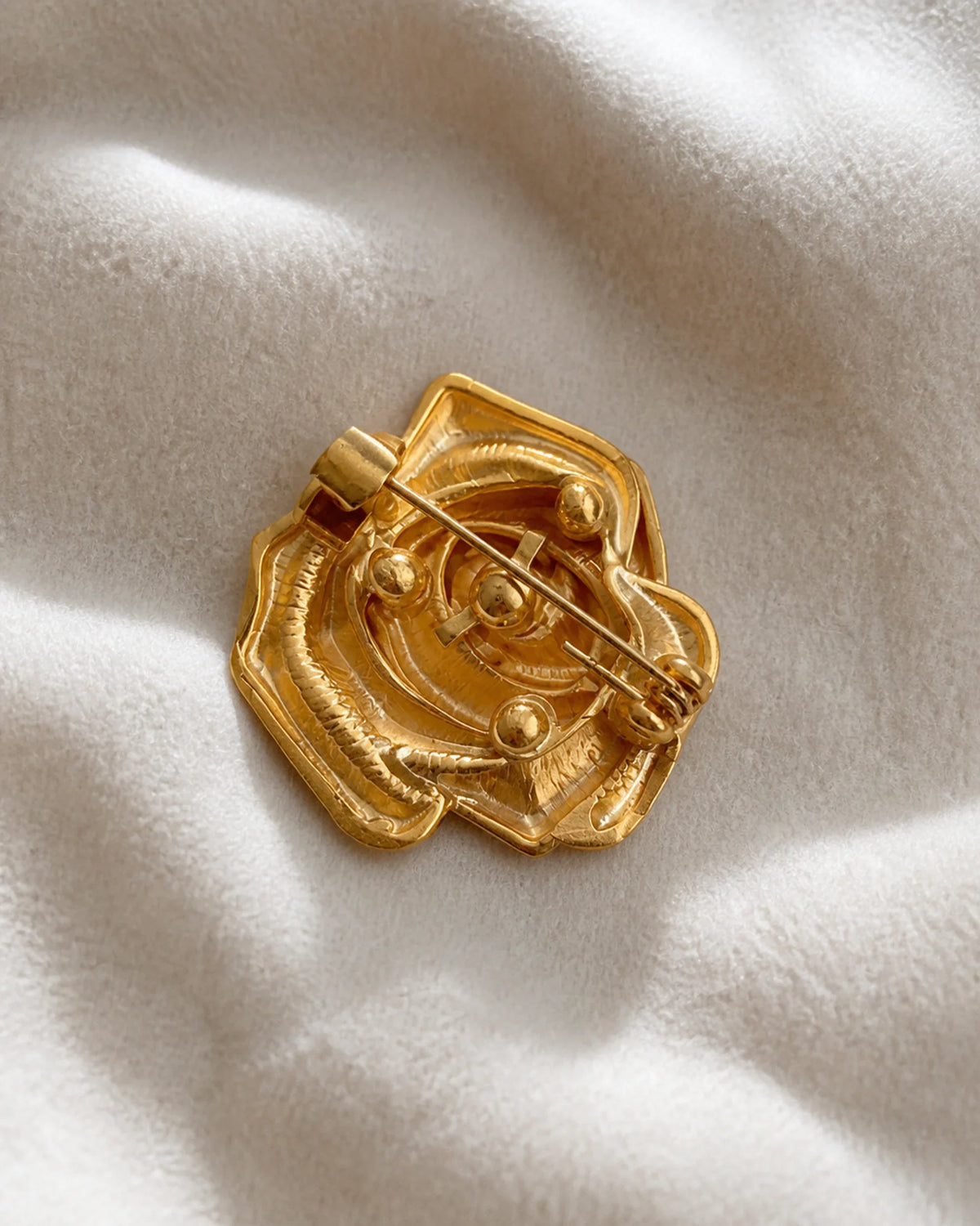 Back of the Taimi Mini Gold Camellia Brooch showing its pin stem, hinge and safety clasp on ivory fabric