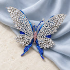 Tilda openwork butterfly brooch resting on pale blue-gray silk and ivory stone.