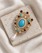 Tove Turquoise-Blue Scroll Drop Brooch — front view on a stone tile and ivory linen