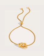 Lovi Adjustable Gold Heart Knot Bracelet on a soft warm grey background