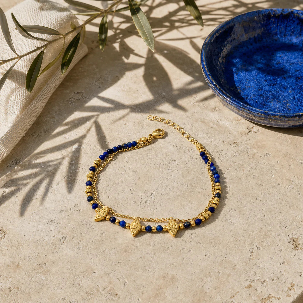 Nila Lapis Charm Bracelet displayed on sunlit travertine beside a cobalt ceramic dish
