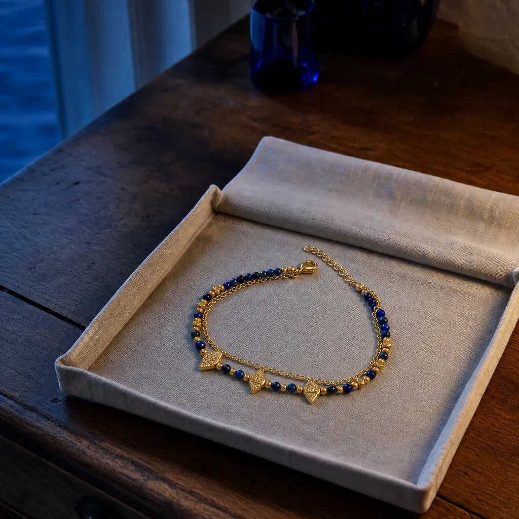 Nila Lapis Charm Bracelet resting in an ivory linen jewelry tray at blue hour