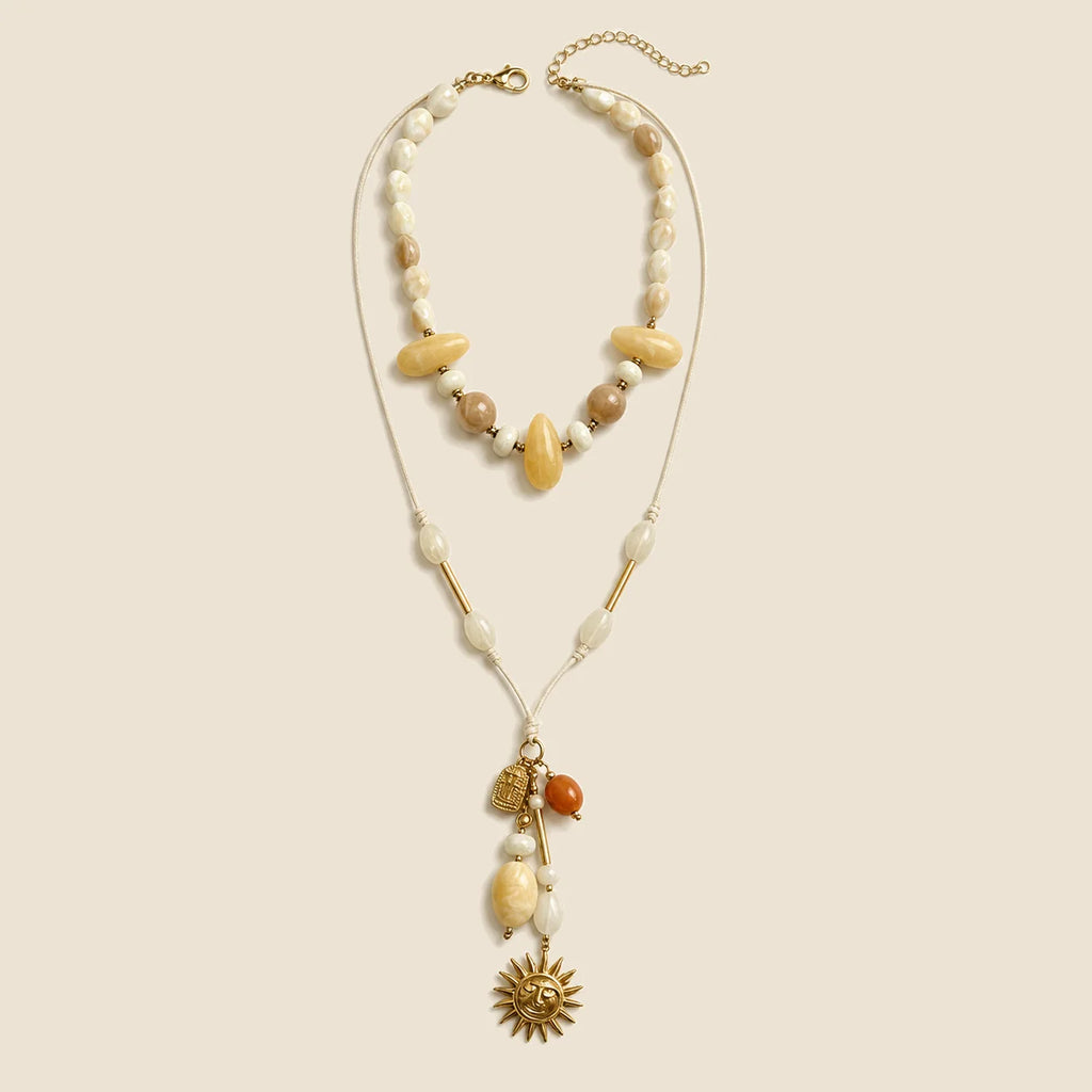 Solara Layered Talisman Necklace displayed in full on an exact #EDE3D4 background
