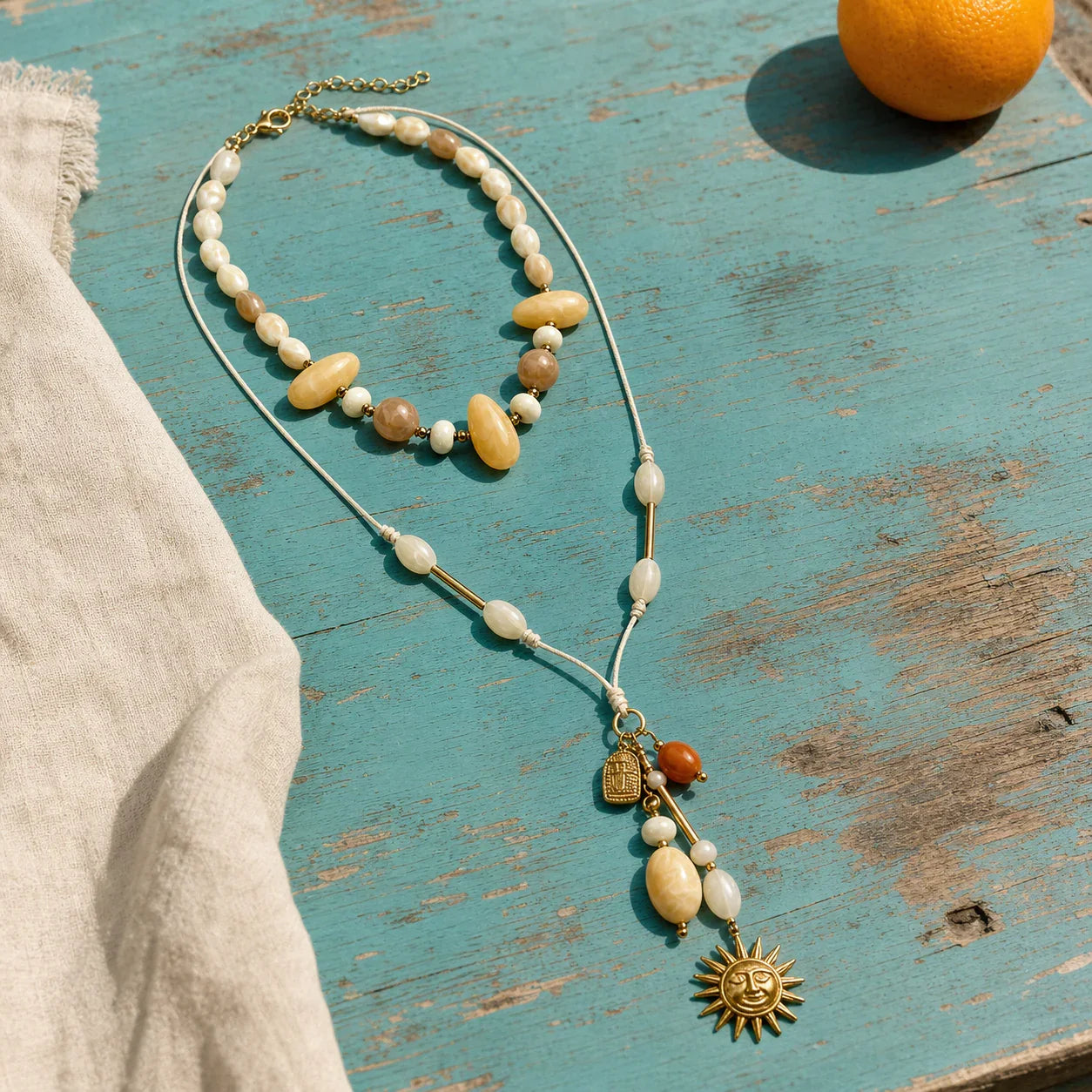 Solara Layered Talisman Necklace arranged on a weathered turquoise table in sunlight