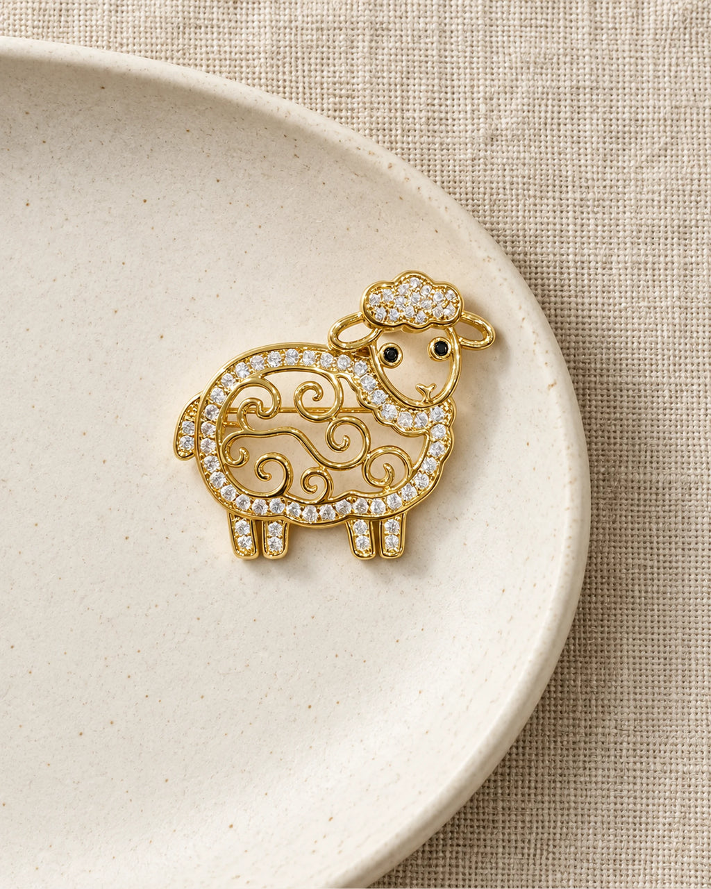 Ulla Openwork Crystal Sheep Brooch on an ivory ceramic dish and linen