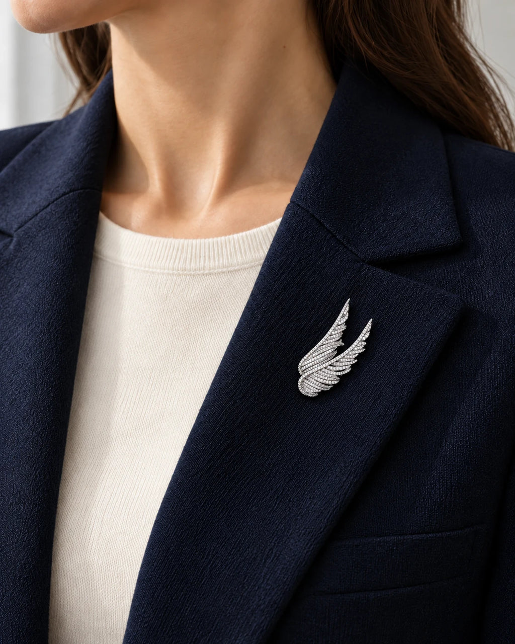 Silver Vinga twin wing brooch pinned to a navy blazer lapel above a white knit top.