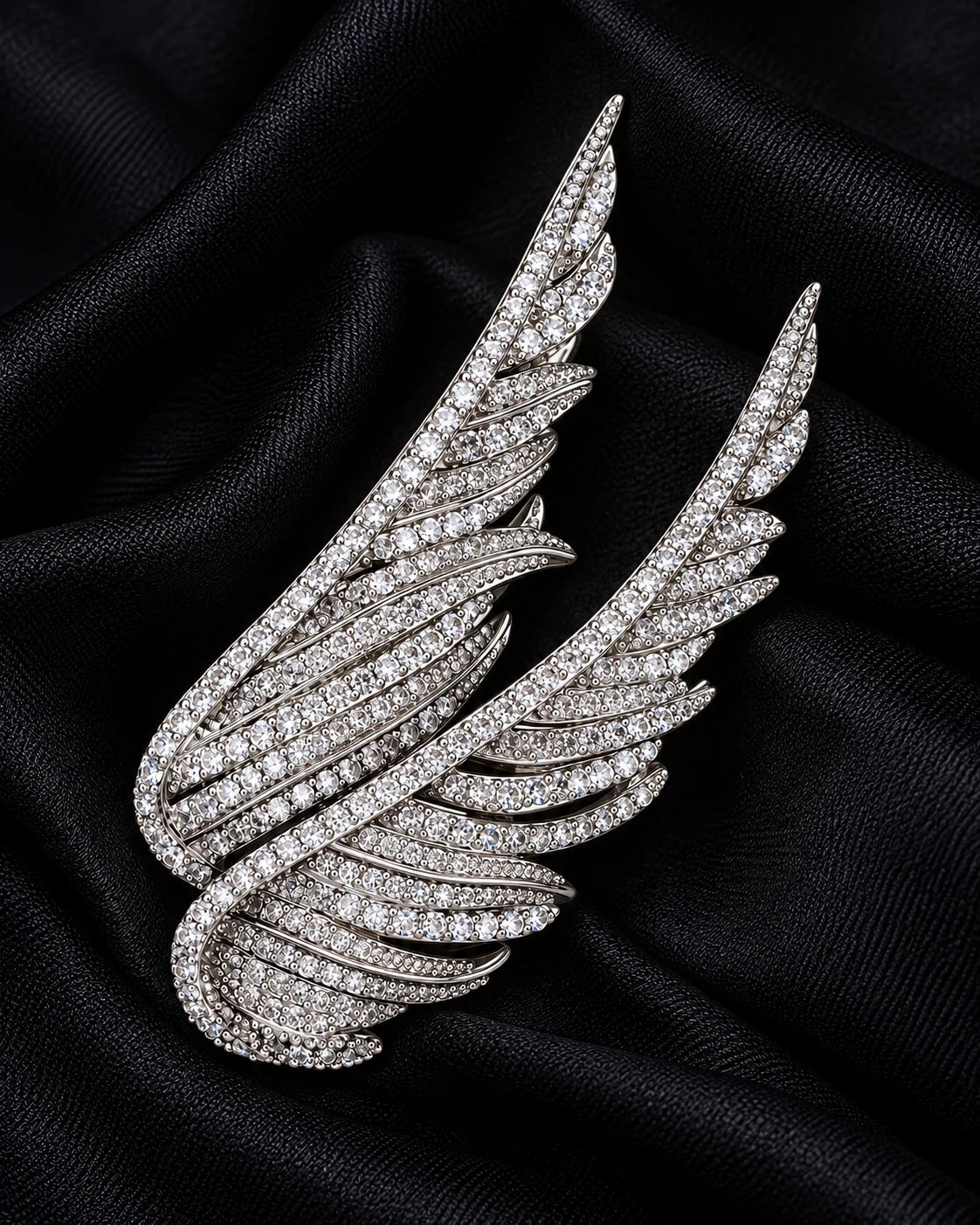 Silver Vinga twin wing brooch resting on softly folded black cloth.