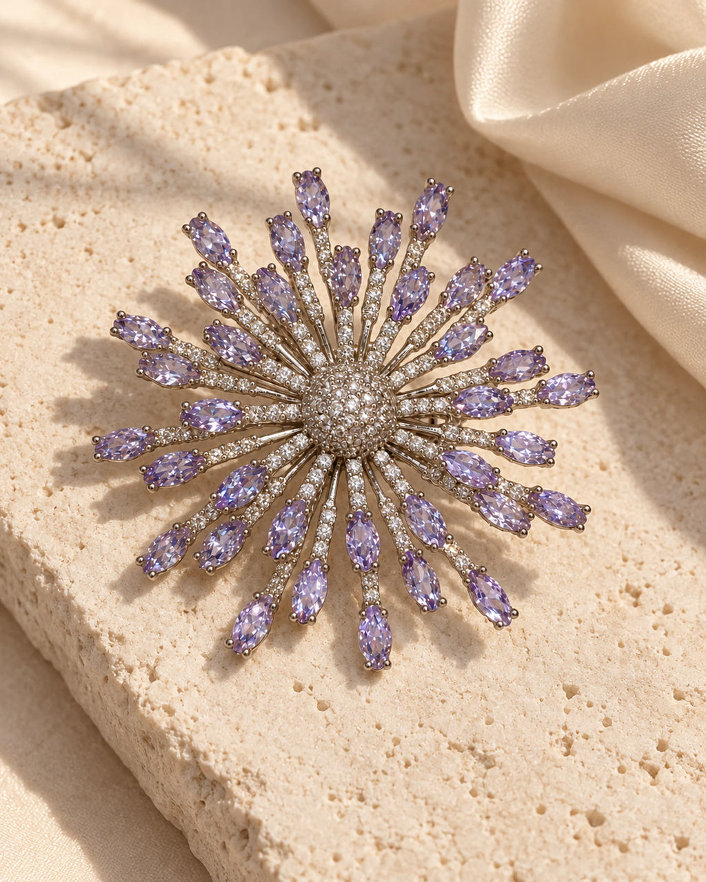 Viola lavender zircon starburst brooch on pale limestone beside ivory silk