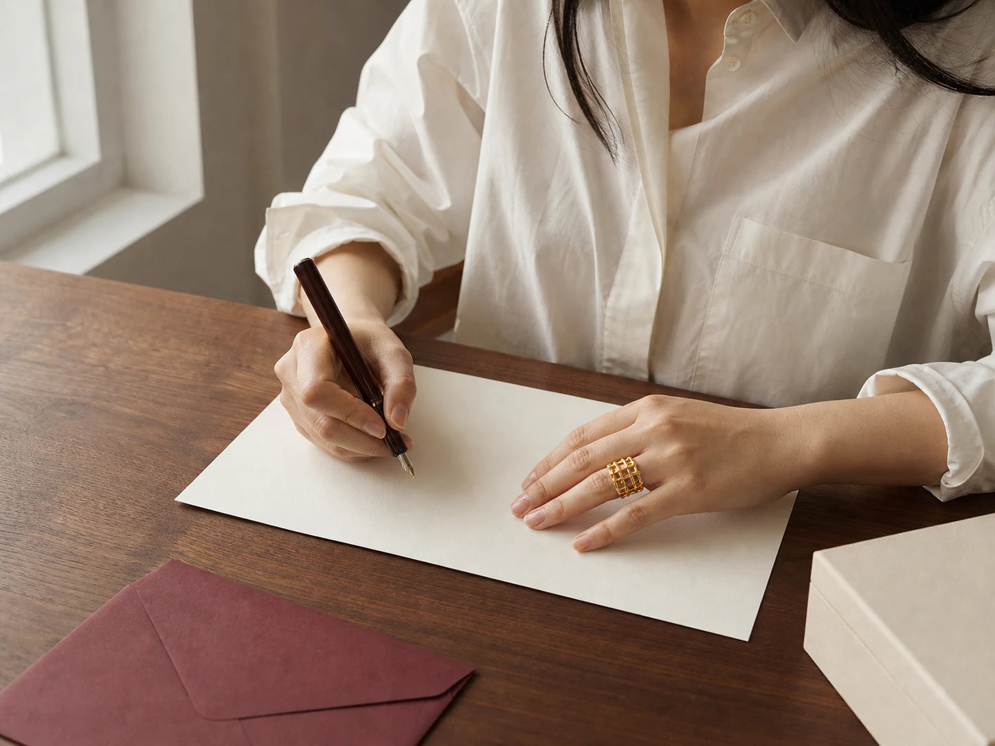 Person writing at a walnut desk while wearing the Trellis Light Wide Ring