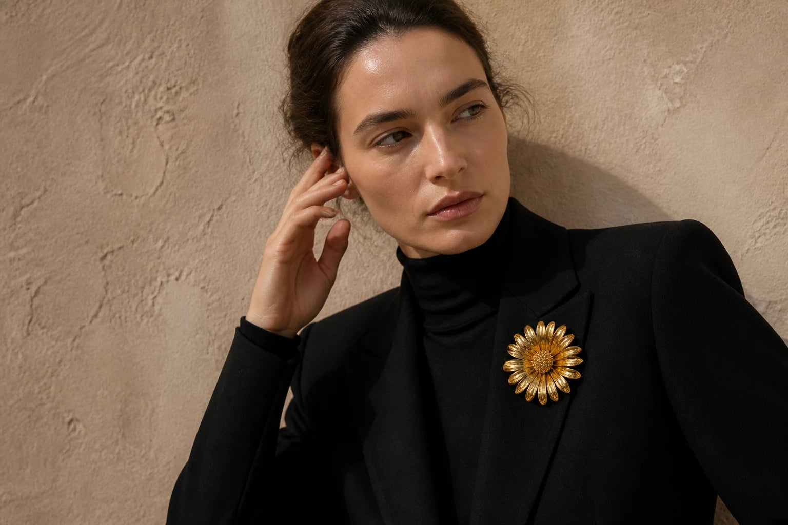 Model wearing the gold Aurinko Bloom Brooch on a structured black blazer